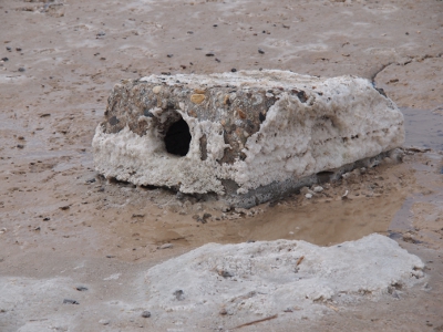 [Cement chunk that looks like it had a pipe running through it at one time (there's a cylindrical hole in the center). Most of the outsides of it are caked with at least a half inch of salt buildup.]